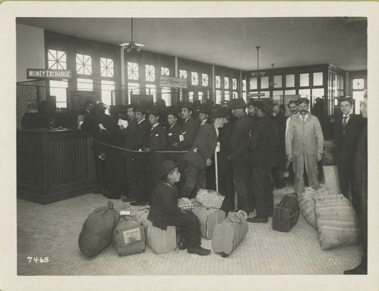 Ready for travel and going north, south and west. Immigrants with baggage lined up at teller's windows marked money exchange.