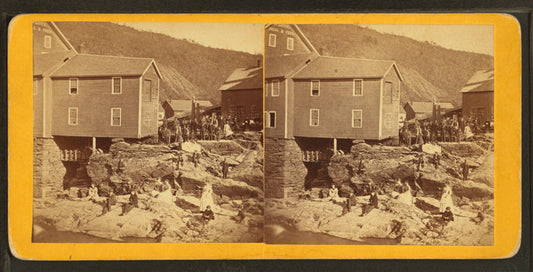 People on rocks near river and buildings damaged by flood.